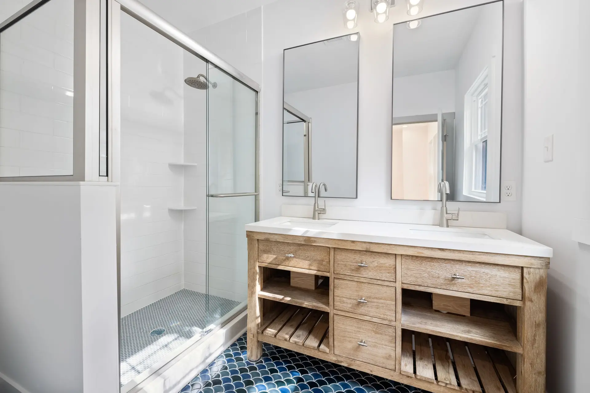 Bathroom with a glass shower and a double wood vanity under two mirrors