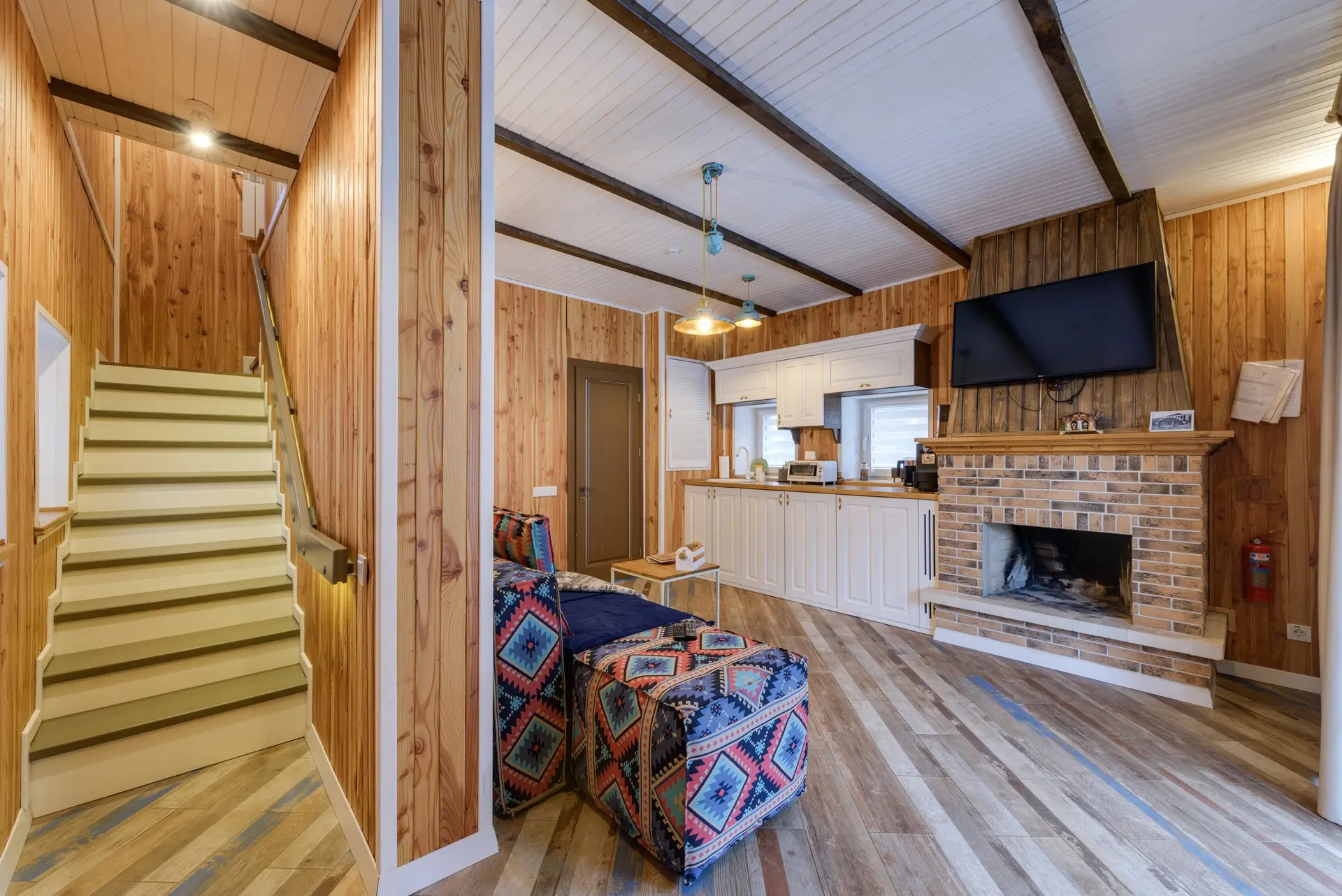 Wood-paneled room with exposed rafters, a brick fireplace and a stair