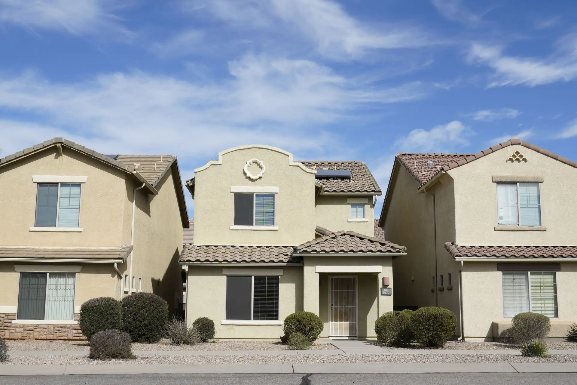 Three two-story stucco houses side by side under a clear sky