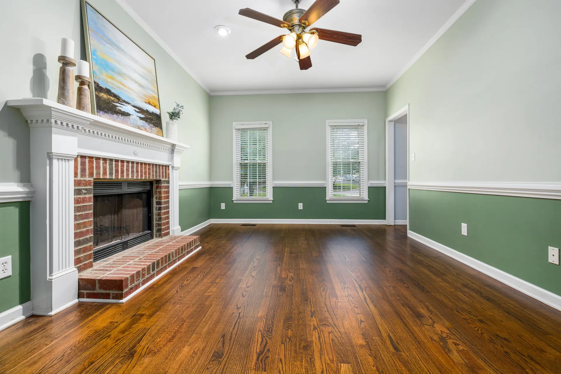 Empty living room with a brick fireplace, two-tone walls and wood floors